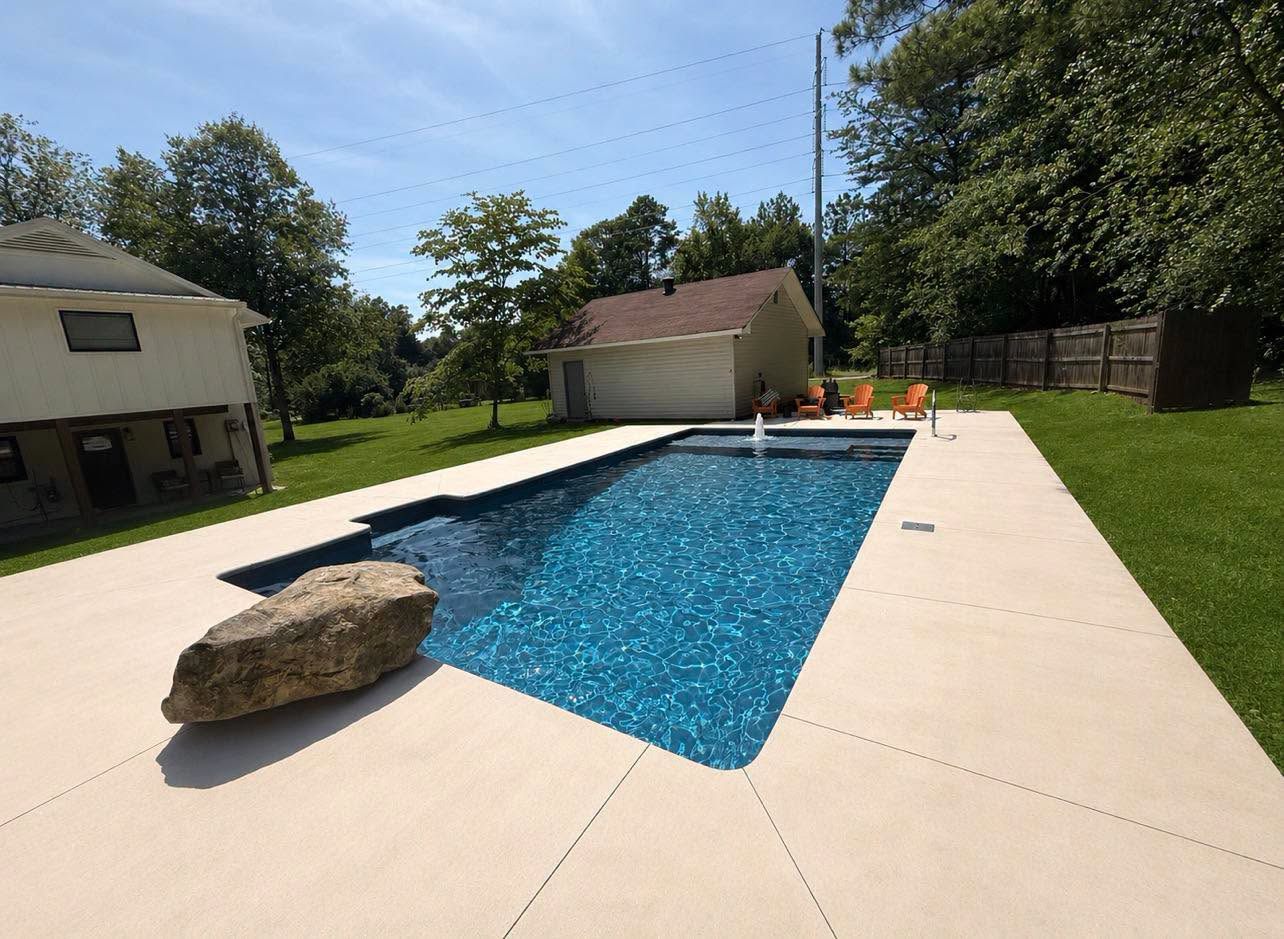 Rectangular pool with a tanning ledge, feature boulder and wide sand-toned concrete deck