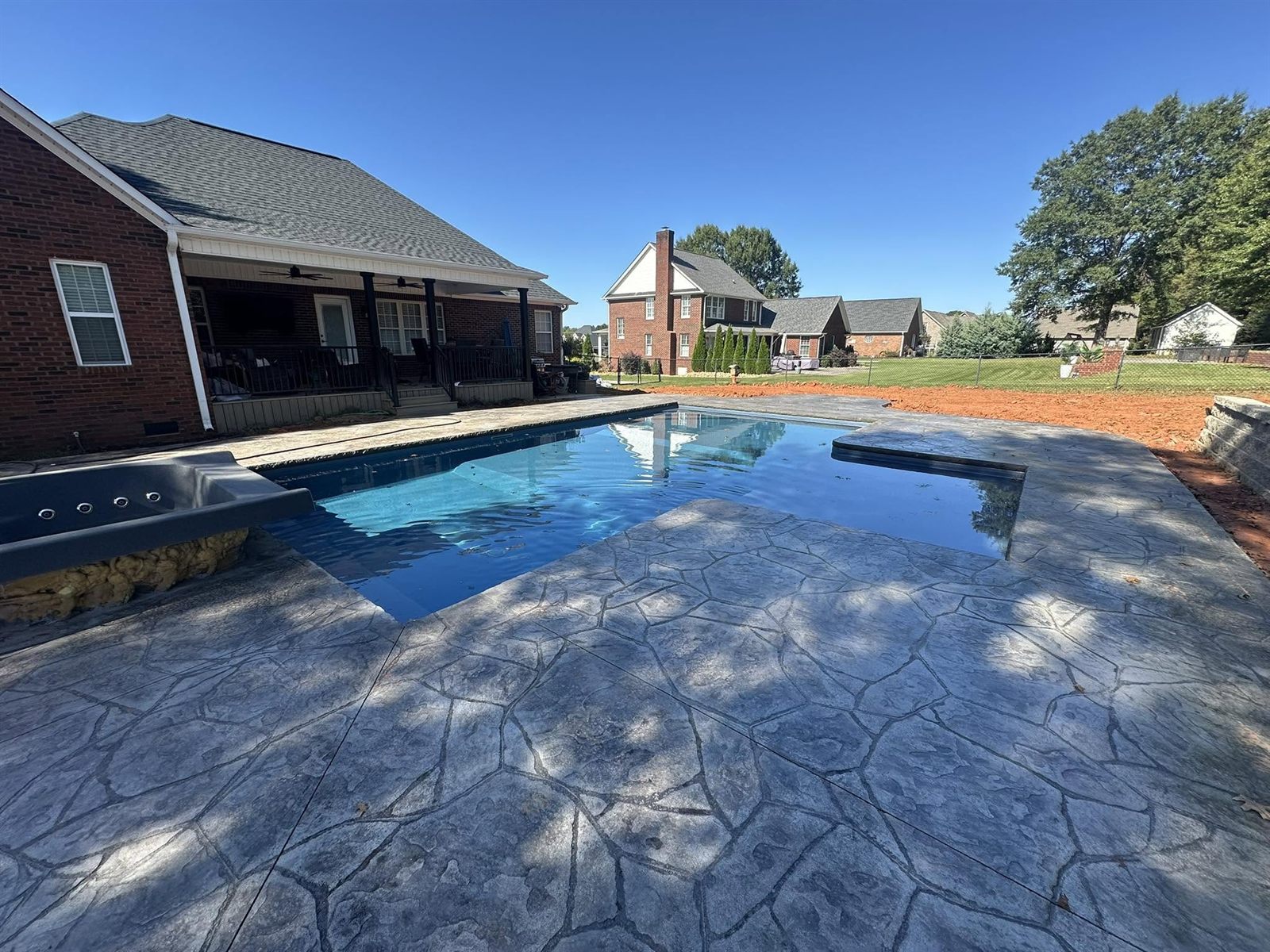 In-ground pool with an attached spa surrounded by stamped concrete decking at a brick home